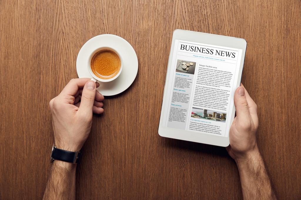vista recortada del hombre sosteniendo tableta digital con noticias de negocios en la pantalla y taza de café
 - Foto, imagen