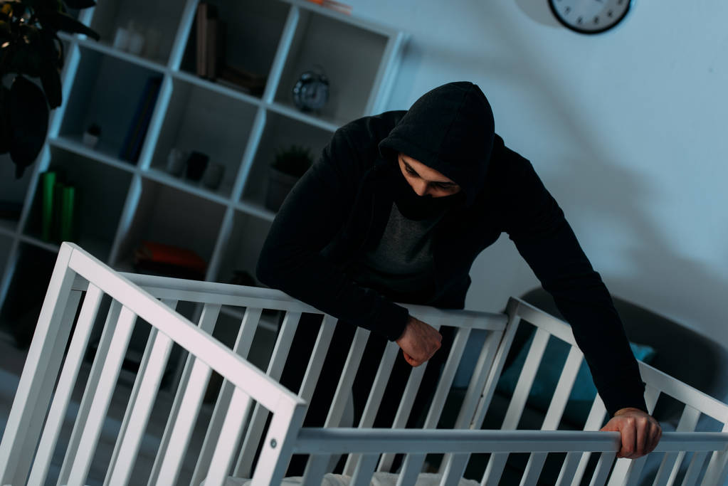 Kidnapper in schwarzer Kleidung steht in dunklem Raum und schaut in Krippe - Foto, Bild