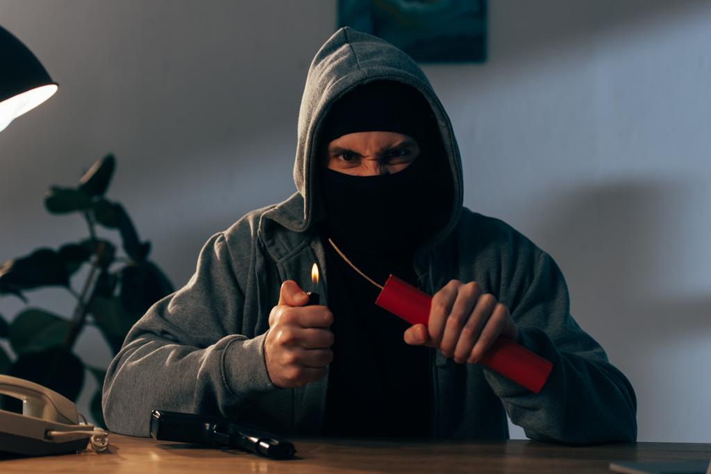 Terrorista enojado en máscara con pistola encendiendo dinamita en la habitación
 - Foto, imagen