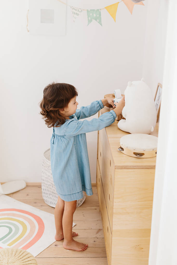 Little girl wearing light blue dress playing in children room scandinavian style. - Photo, Image