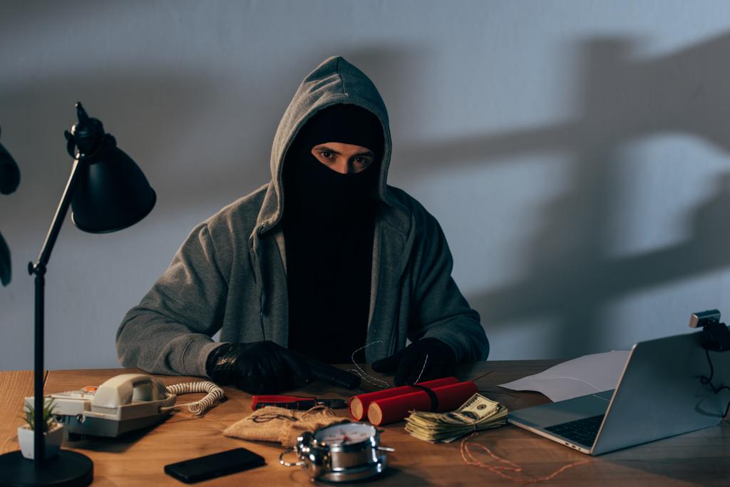 Verbrecher in Maske mit Pistole und Dynamit sitzt am Tisch und schaut in die Kamera - Foto, Bild