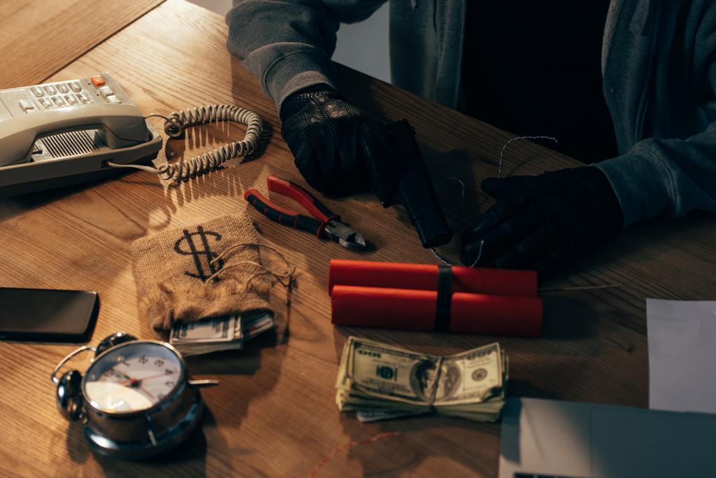 Обрізаний погляд на злочинця в чорних рукавицях з пістолетом, динамітом і доларовими банкнотами
 - Фото, зображення