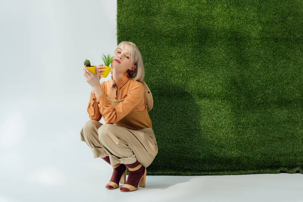bella ragazza alla moda che tiene vasi di fiori su grigio con erba verde
  - Foto, immagini
