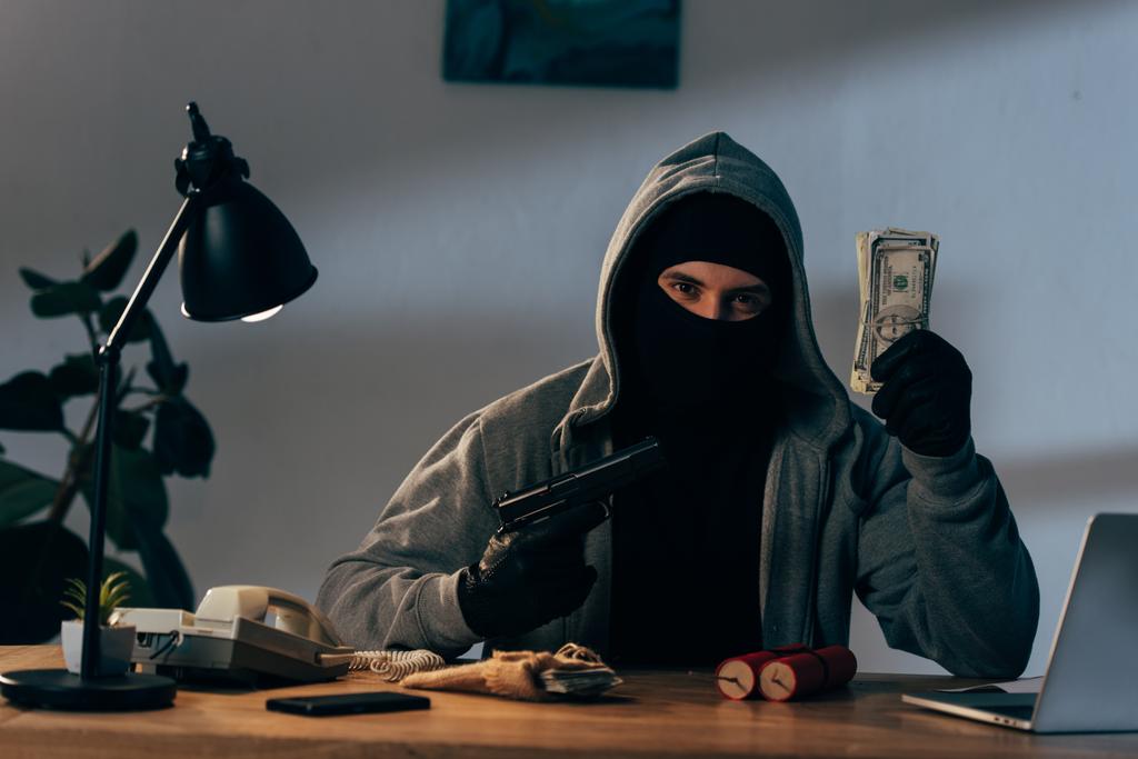 Terrorist in mask and gloves holding gun and dollar banknotes - Photo, Image