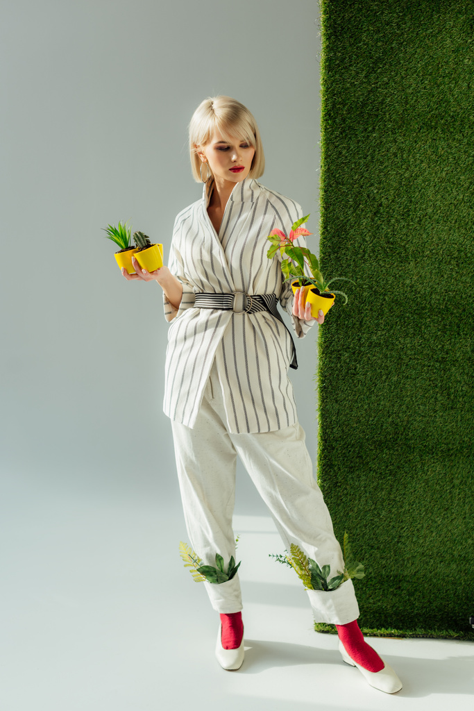 belle fille élégante posant tout en tenant des pots de fleurs sur gris avec de l'herbe verte
  - Photo, image