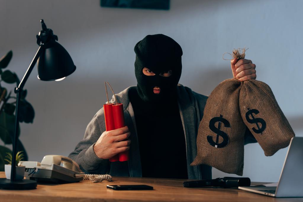 Terrorista en máscara sosteniendo dinamita y bolsas de dinero en la habitación
 - Foto, imagen