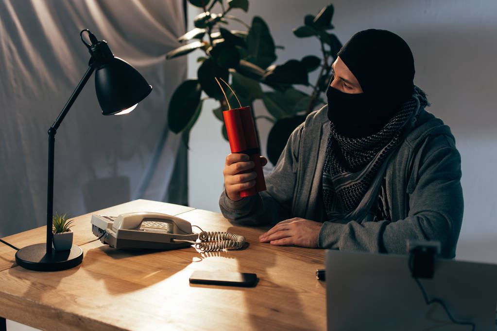 Terrorista en máscara sentado en la habitación y sosteniendo dinamita
 - Foto, imagen
