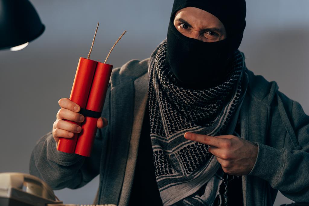 Агрессивный террорист показывает пальцем на динамит и смотрит в камеру
 - Фото, изображение