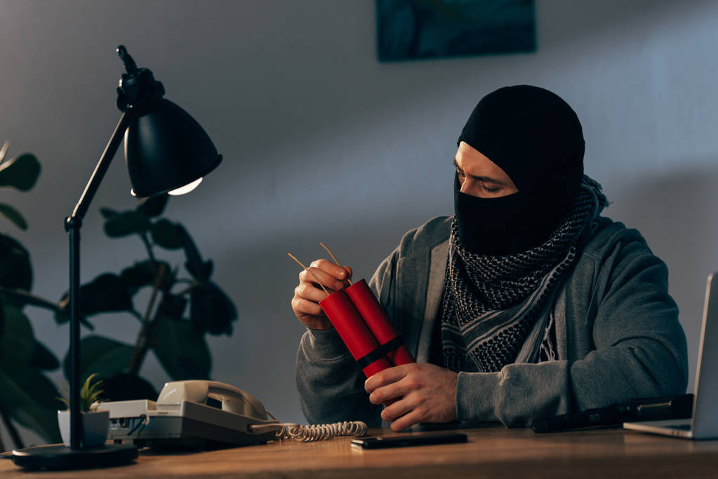 Terroriste masqué avec dynamite assis à table dans la chambre
 - Photo, image