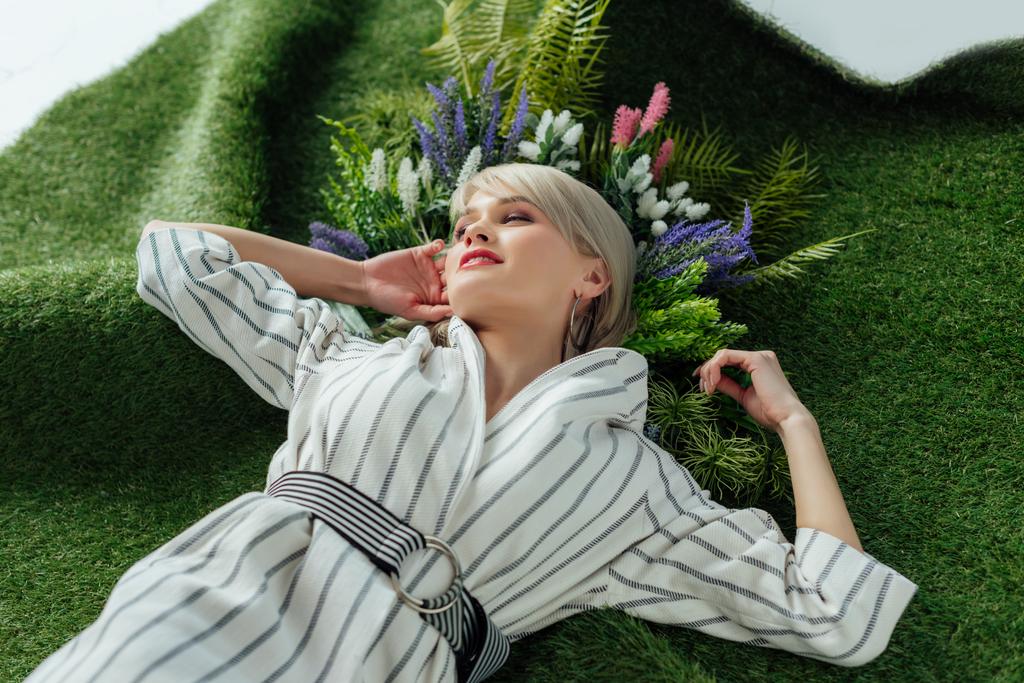 красива стильна дівчина з закритими очима позує на штучній траві з папороті і квітами
 - Фото, зображення