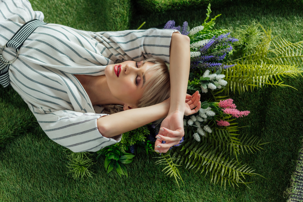 魅力的なスタイリッシュな女の子の目を閉じたシダと花を人工芝に横たわって - 写真・画像