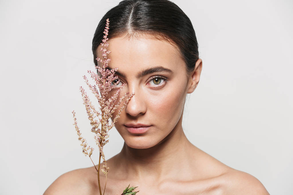 Здоровий приваблива брюнетка жінка стоїть ізольовано тримає квіткову рослину біля її обличчя
 - Фото, зображення
