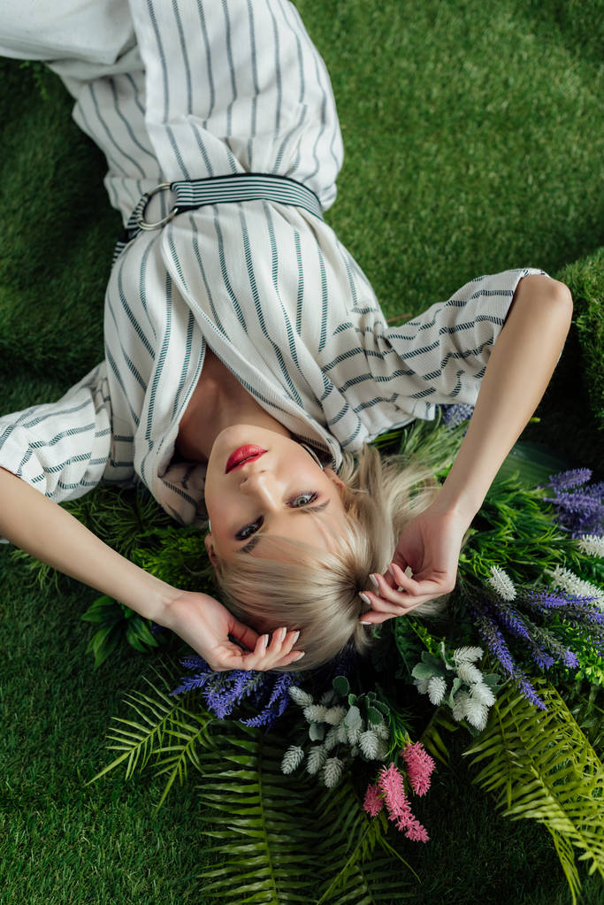 ylhäältä kaunis tyylikäs tyttö makaa tekonurmella saniainen ja kukkia
 - Valokuva, kuva