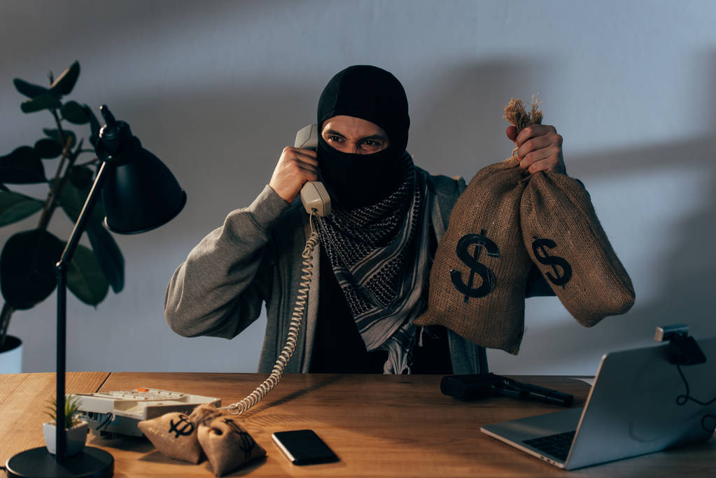 Boos terrorist holding Geldzak met dollartekens en praten over de telefoon - Foto, afbeelding