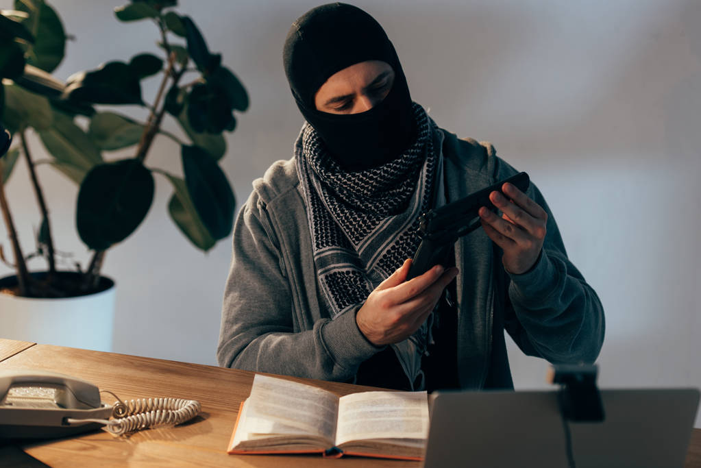 Terroriste pensif masqué noir regardant une arme dans une pièce
 - Photo, image