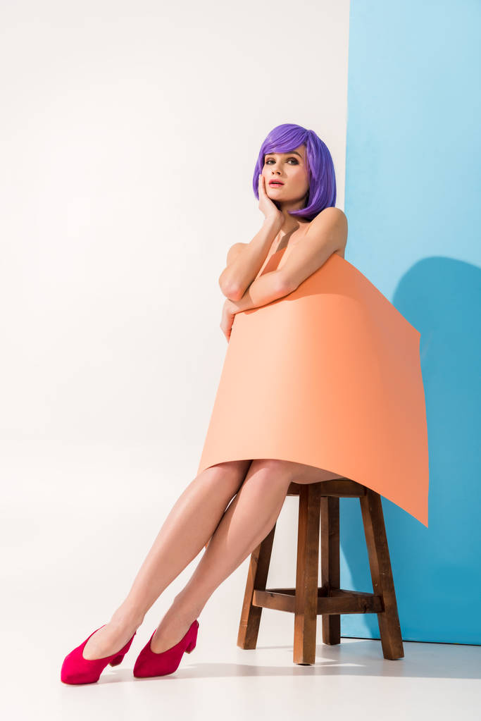 όμορφο κορίτσι με μοβ μαλλιά καλύπτεται στο φύλλο κοραλλιών χαρτί που κάθεται σε καρέκλα, ενώ θέτουν σε μπλε και άσπρο - Φωτογραφία, εικόνα