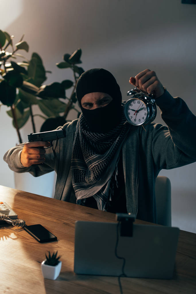 Wütender Terrorist in Maske zielt mit Waffe auf Wecker im Zimmer - Foto, Bild
