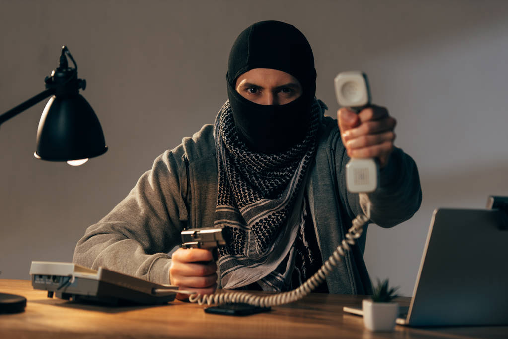 Terrorista enojado con máscara negra sosteniendo pistola y mostrando el auricular a la cámara
 - Foto, imagen