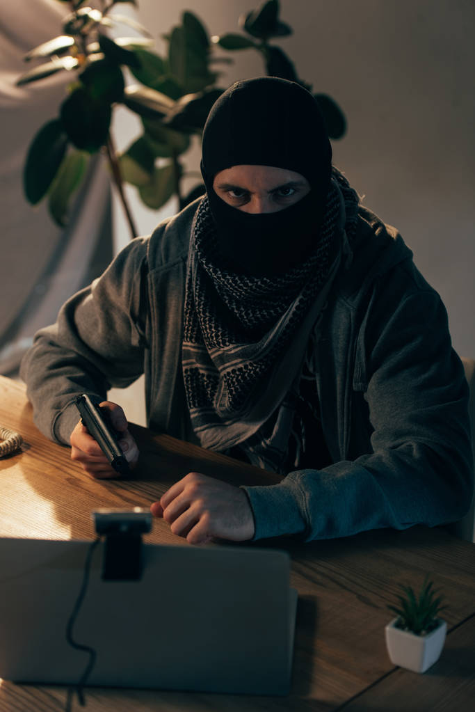 Злой террорист в маске, нацеленный на пистолет и смотрящий в камеру
 - Фото, изображение