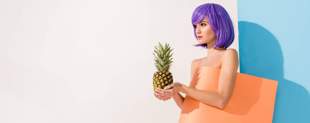 menina bonita com cabelo roxo coberto de folha de papel de coral segurando abacaxi enquanto posando em azul e branco
 - Foto, Imagem