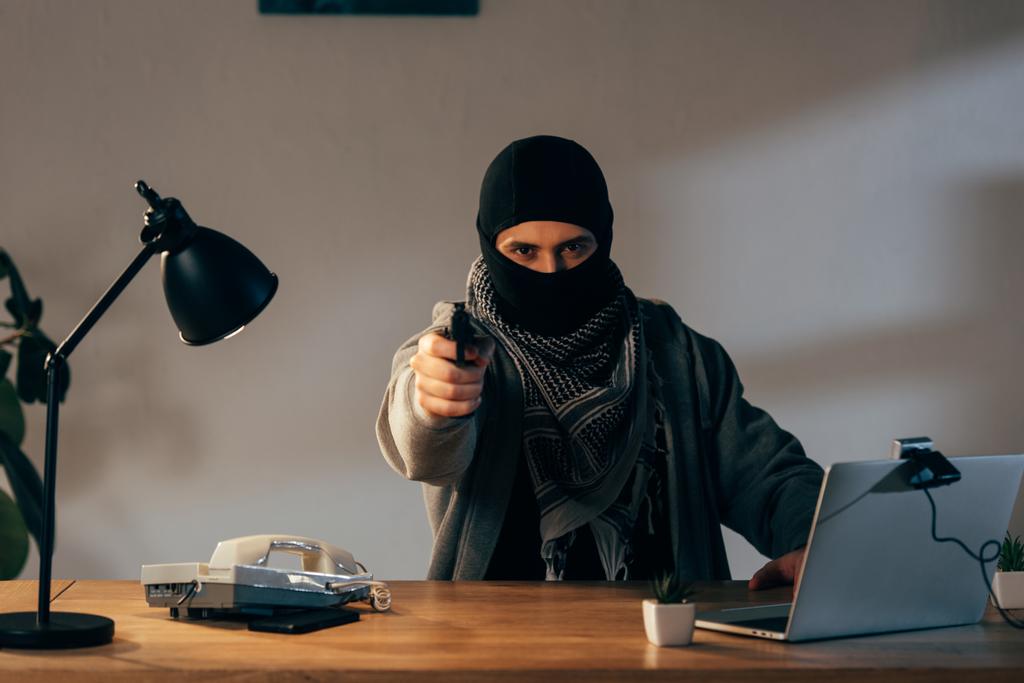 Wütender Terrorist in schwarzer Maske zielt mit Waffe auf Kamera - Foto, Bild