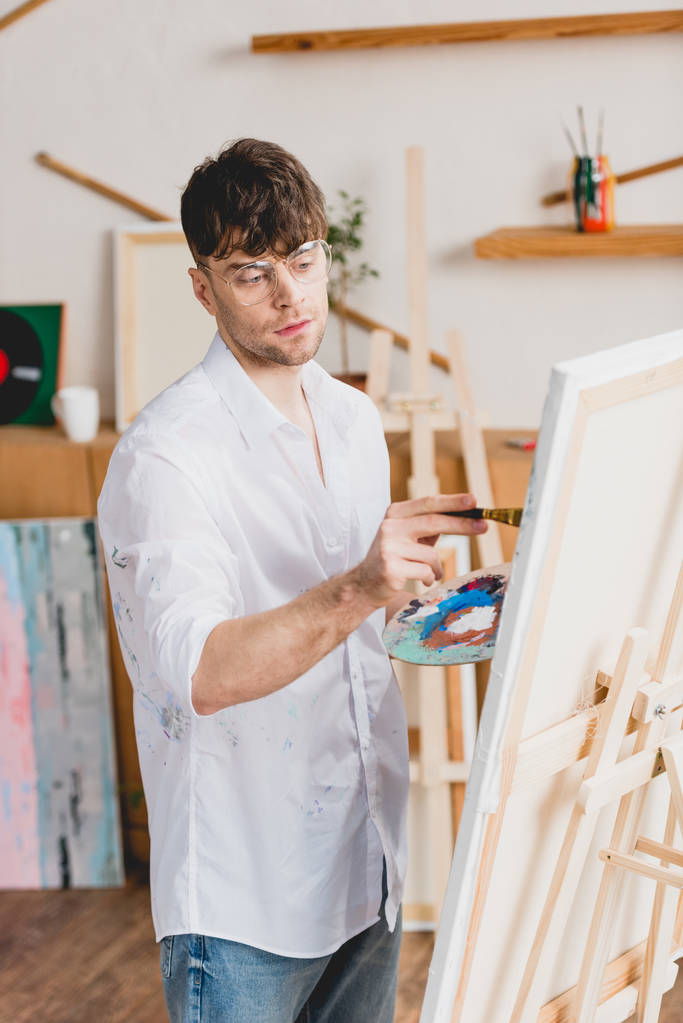 pohledný umělec v bílé košili a brýle, malba na plátně v galerii - Fotografie, Obrázek