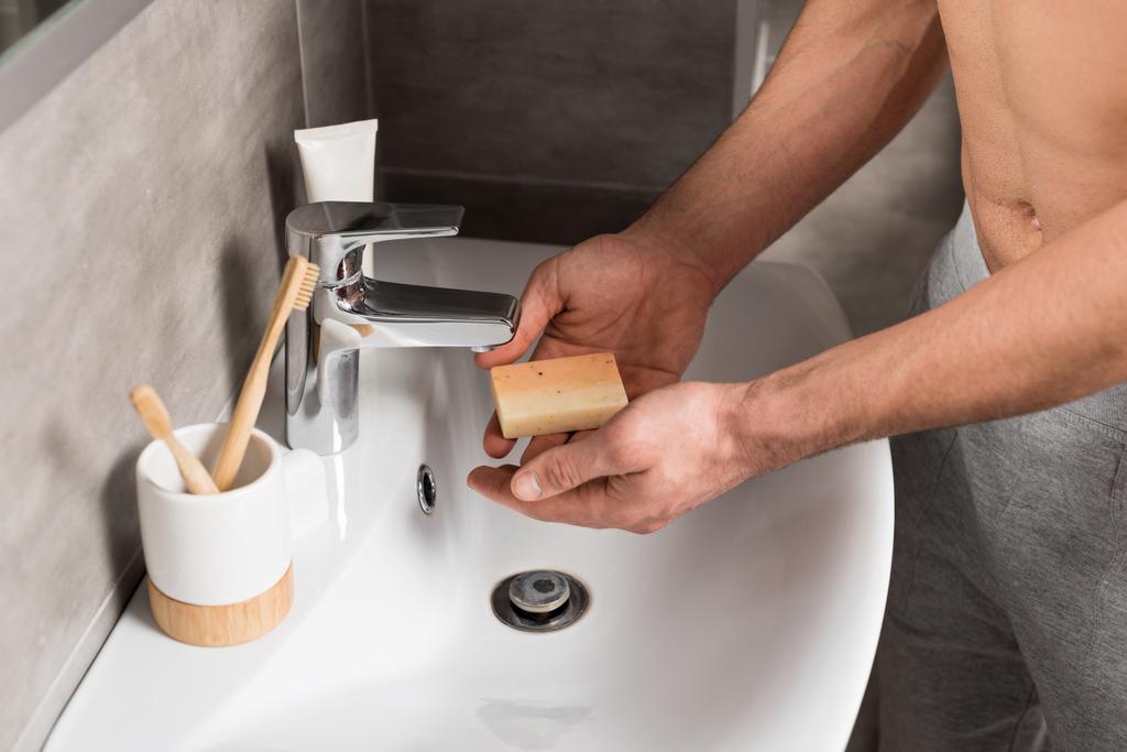 cropped view of man holding soap near sink while standing in bathroom  - Photo, Image