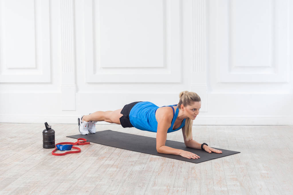 Вид сбоку на мускулистую спортивную сильную атлетичную блондинку в черных шортах и синем топе, стоящую на идеальной позиции локтя, спортивная и здоровая концепция
 - Фото, изображение
