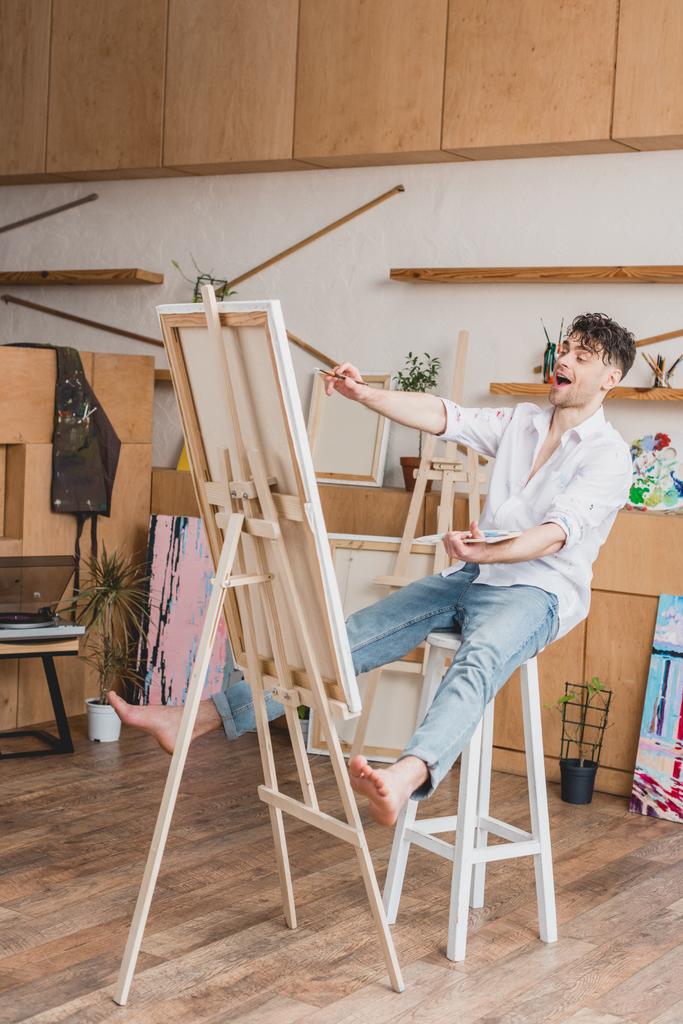 excited artist sitting on high chair at easel with canvas - Photo, Image