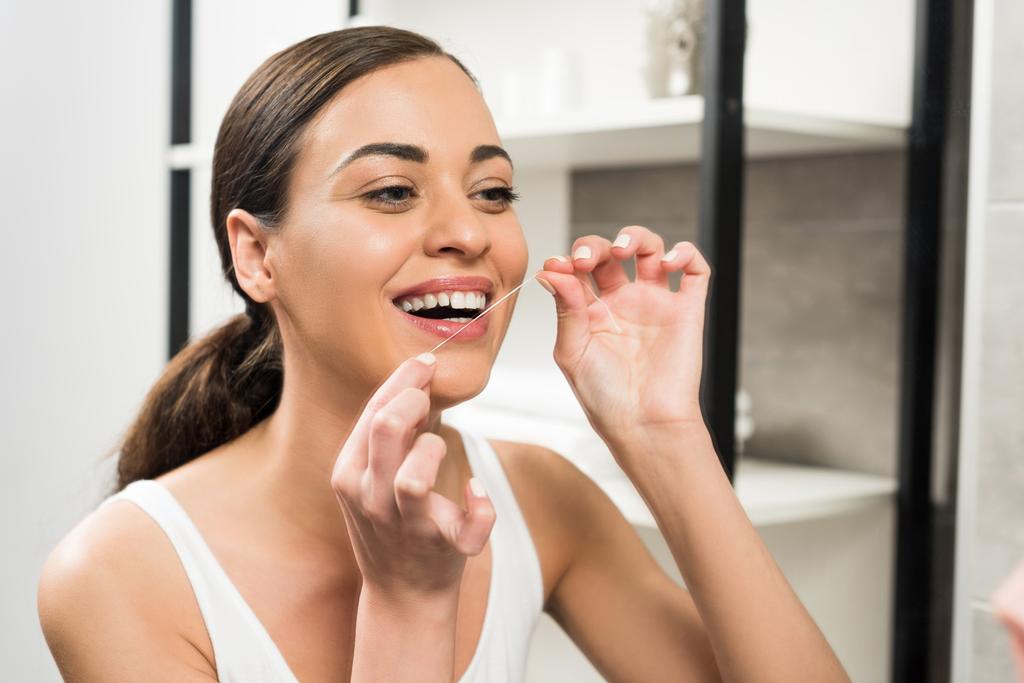 Mujer morena alegre usando hilo dental en el baño  - Foto, imagen