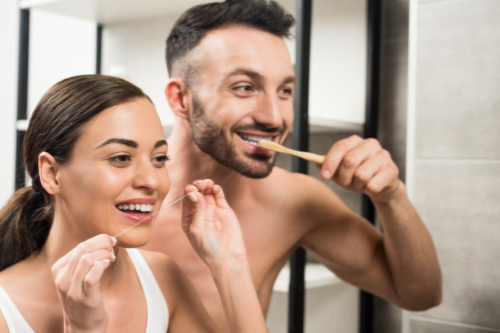 ひげを生やした彼氏のガール フレンドが浴室でデンタルフロスを使用して近くの歯を磨く  - 写真・画像