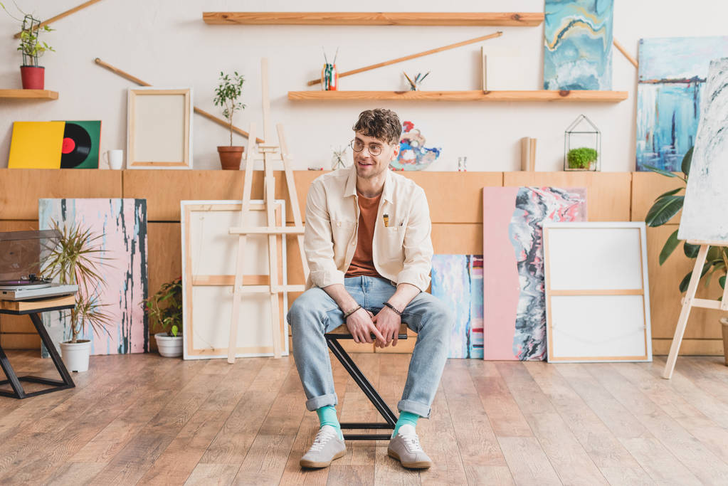 handsome smiling artist sitting on chair in spacious light gallery - Photo, Image