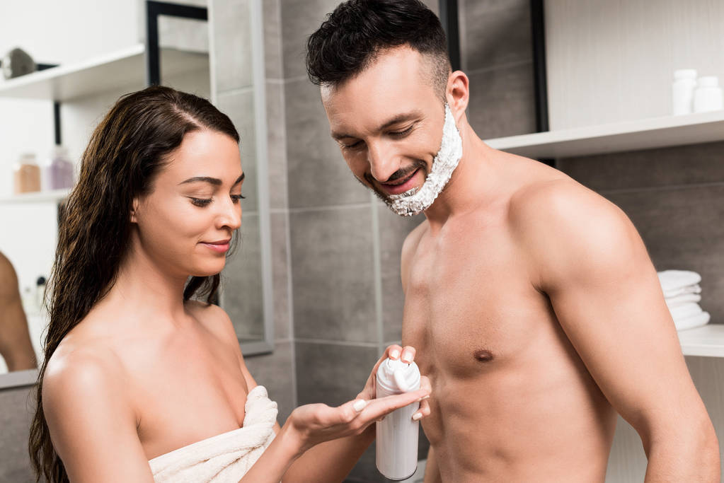 komea parrakas mies, jolla on partavaahto kasvoilla katsomalla houkuttelevan tyttöystävän kättä kylpyhuoneessa
  - Valokuva, kuva