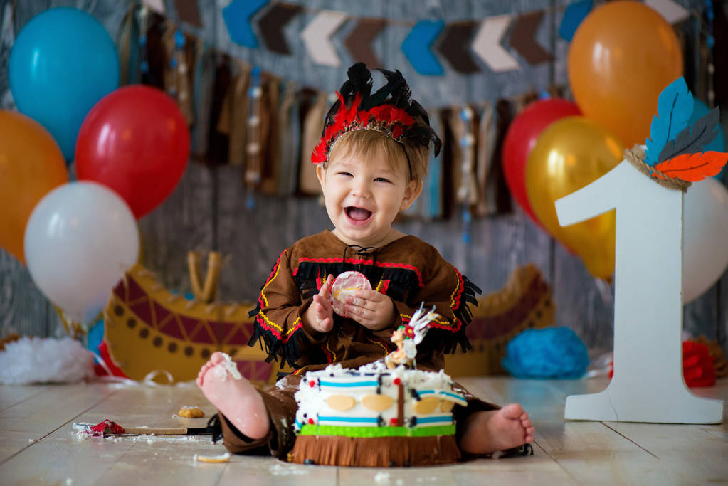 beetje schattige jongen in kostuum van American Indian Apache Chief zit en smash cake. Kinder vakantie, gelukkig verjaardag 1 jaar, foto zone decoratie - Foto, afbeelding