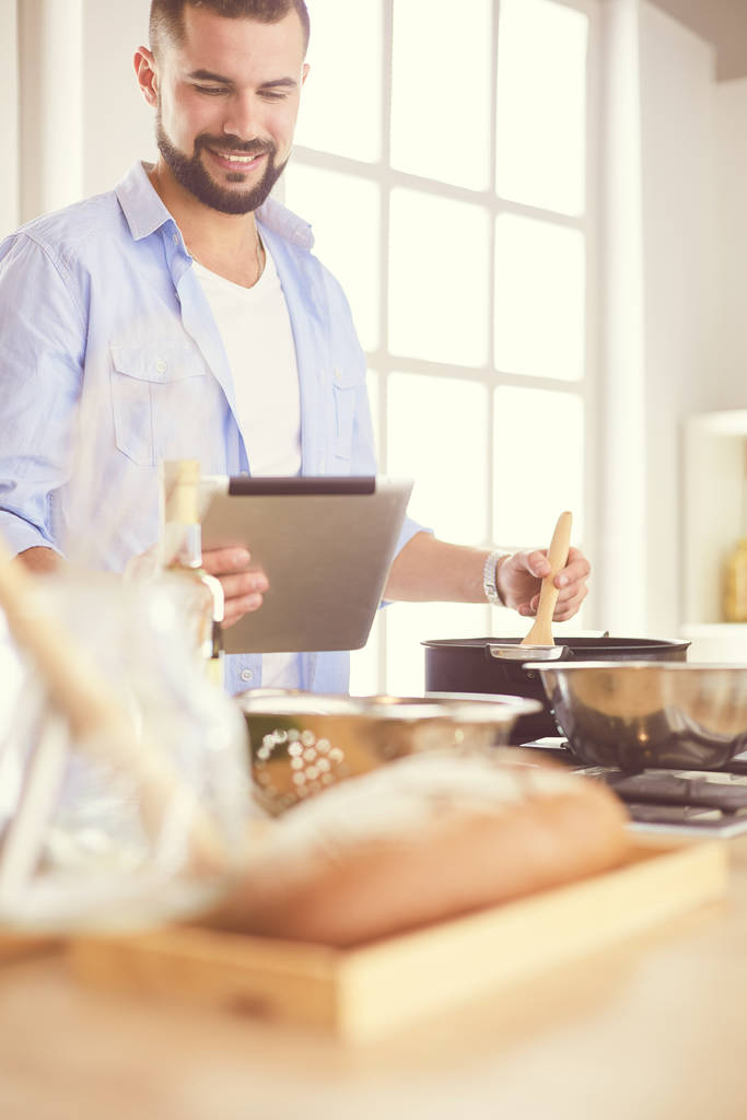 Mann folgt Rezept auf digitalem Tablet und kocht leckeres und gesundes Essen in der heimischen Küche - Foto, Bild