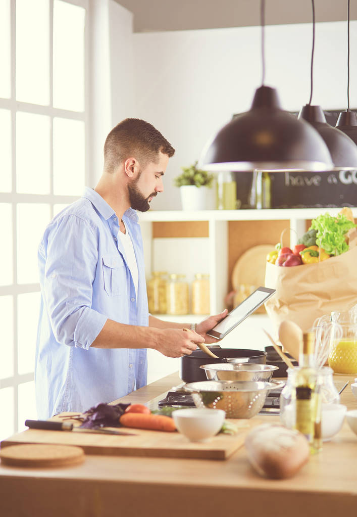 デジタルタブレット上のレシピに従う男と自宅でキッチンでおいしいと健康食品を調理 - 写真・画像