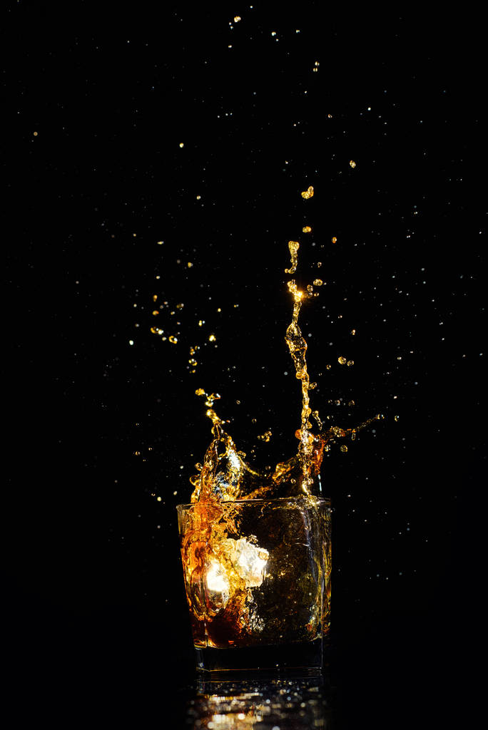 Colpo isolato di whisky con spruzzata su sfondo nero - Foto, immagini