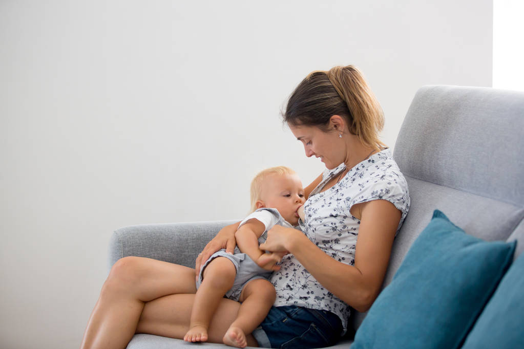 Νεαρή μητέρα, κάθεται στο σπίτι στο ηλιόλουστο σαλόνι, αγκαλιά εξυπνάδα - Φωτογραφία, εικόνα