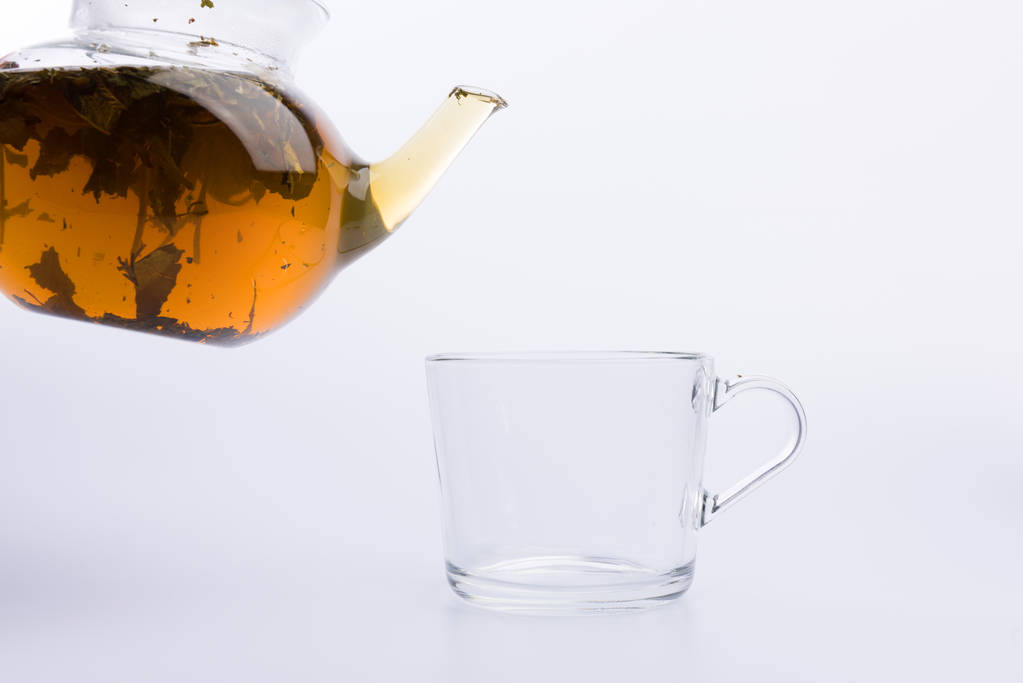 Tetera de vidrio vertiendo té verde en la taza aislada en blanco
 - Foto, imagen