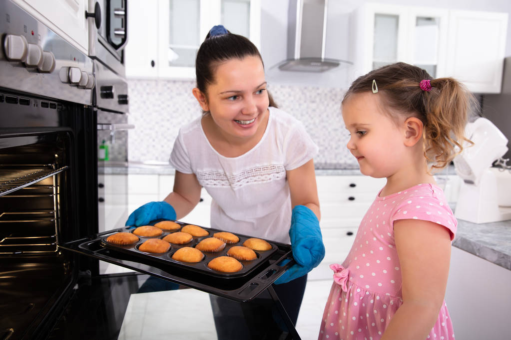 Kızı mutfakta bakarak süre genç anne Holding Cupcake tepsisi - Fotoğraf, Görsel