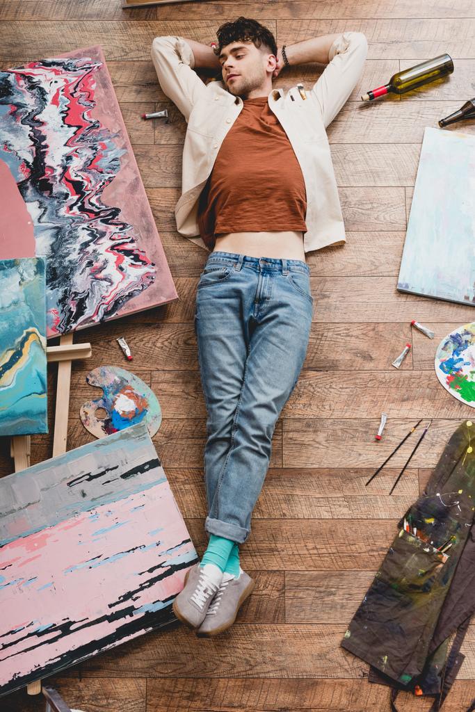 bovenaanzicht van moe kunstenaar slapen op de vloer in schilderij studio - Foto, afbeelding