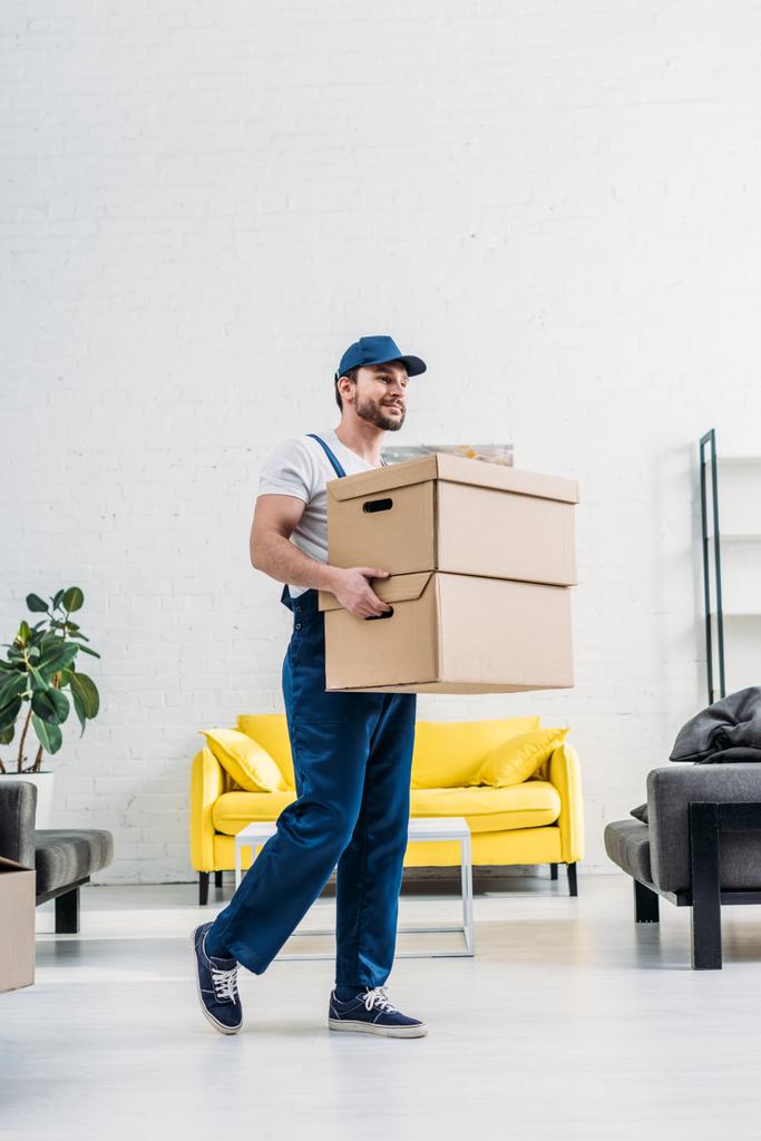 mover in uniform vervoer kartonnen dozen in modern appartement - Foto, afbeelding