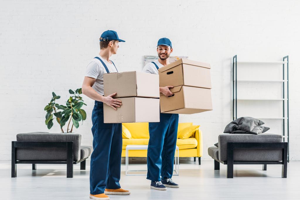 dos mudanzas en uniforme llevando cajas de cartón en apartamento moderno
 - Foto, Imagen