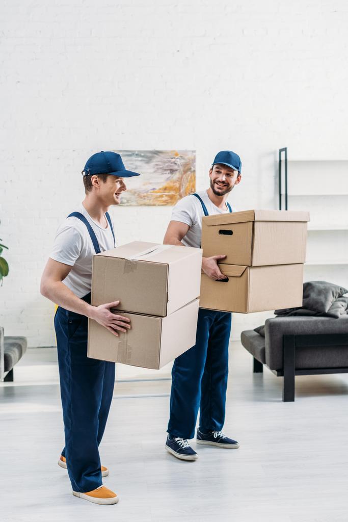 два улыбающихся грузчика в форме несут картонные коробки в квартире
 - Фото, изображение