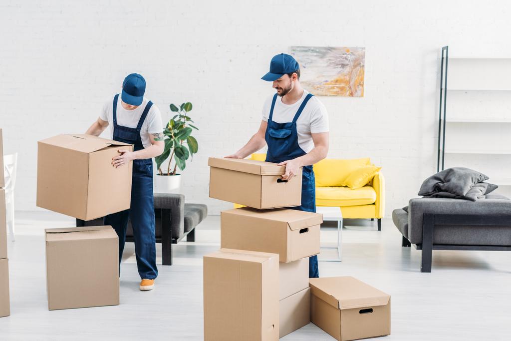 dos mudanzas en uniforme llevando cajas de cartón en apartamento moderno
 - Foto, Imagen