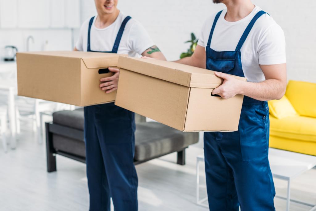 обрезанный вид на двух грузчиков, перевозящих картонные коробки в квартире
 - Фото, изображение