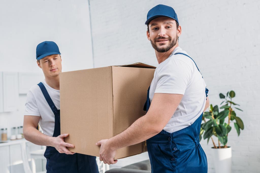 two handsome movers transporting cardboard box in apartment - Photo, Image