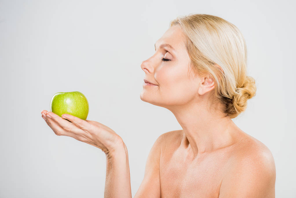 vista laterale di bella donna matura con gli occhi chiusi tenendo mela matura su sfondo grigio
  - Foto, immagini