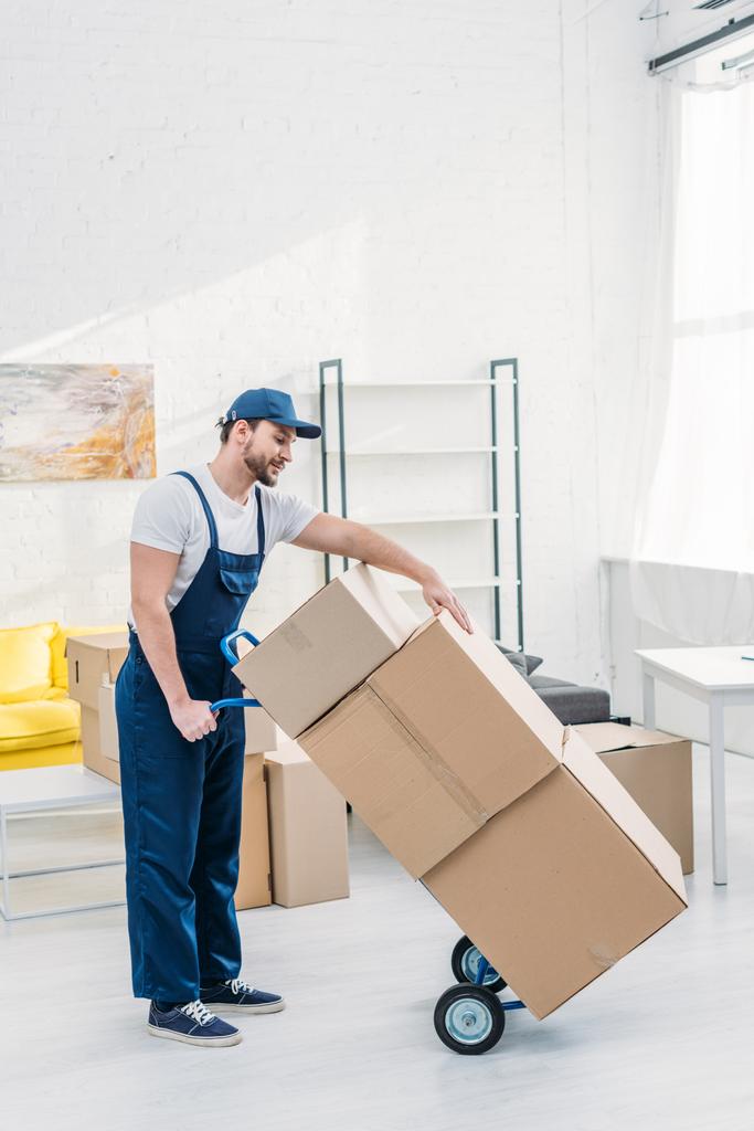 mudanza en uniforme transportando cajas de cartón en camión de mano en apartamento con espacio de copia
 - Foto, Imagen