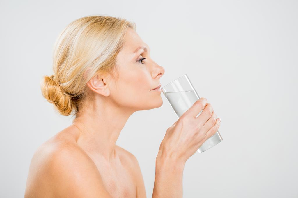 боковой вид зрелой женщины, пьющей воду из стекла, изолированного на сером
  - Фото, изображение